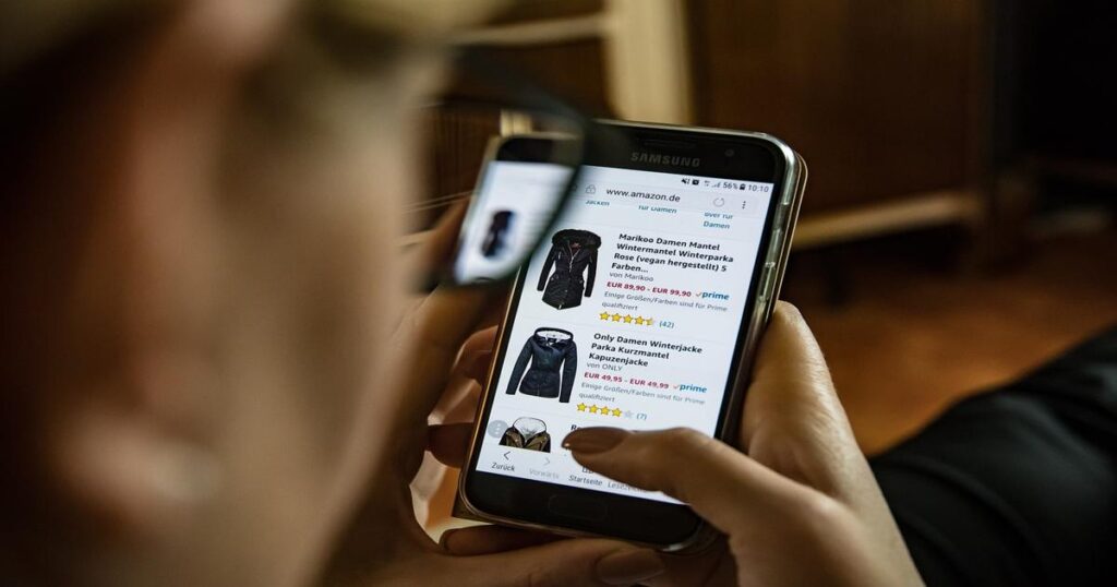 uma mulher de óculos olhando para a tela do celular na qual visualiza roupas em um e-commerce