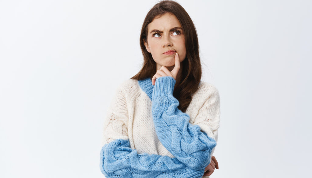 Mulher jovem com expressão pensativa, olhando para cima, sugerindo reflexão ou dúvida, vestida com um suéter claro. A imagem remete à ideia de questionamento sobre estratégias de grandes vendedores em marketplaces, como Mercado Livre e Amazon, explorando como eles conseguem se destacar e aumentar suas vendas em plataformas on-line.